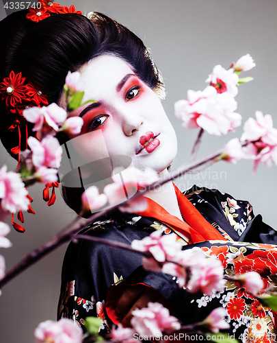 Image of young pretty geisha in kimono with sakura and red decoration des