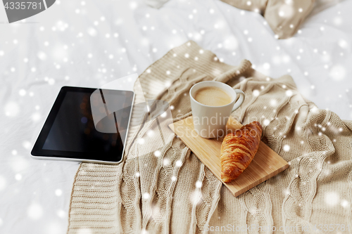 Image of tablet pc, coffee and croissant on bed at home