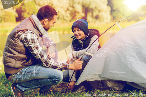 Image of happy father and son setting up tent outdoors