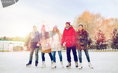 Image of happy friends ice skating on rink outdoors