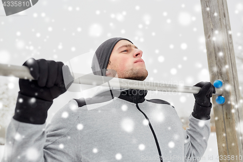 Image of young man exercising on horizontal bar in winter