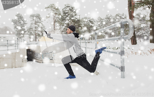 Image of sports man stretching leg at fence in winter