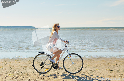 Image of happy woman riding bicycle along summer beach