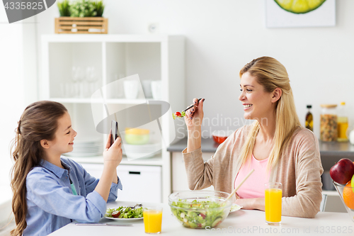 Image of girl photographing mother by smartphone at home