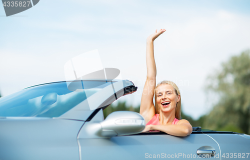 Image of happy young woman in convertible car waving hand