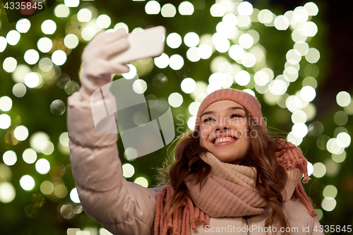 Image of young woman taking selfie over christmas tree