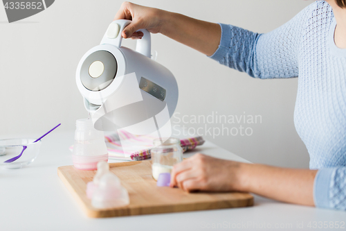 Image of hands with kettle and bottle making baby milk