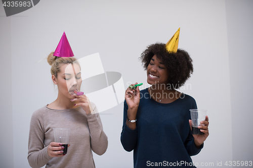 Image of smiling women in party caps blowing to whistles