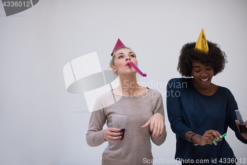 Image of smiling women in party caps blowing to whistles