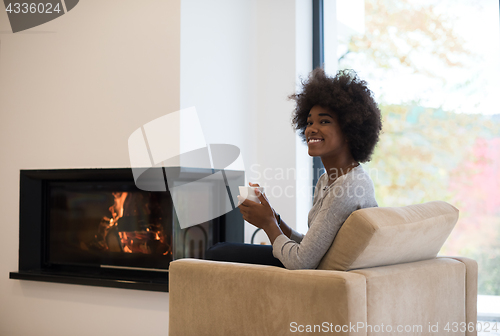 Image of black woman drinking coffee in front of fireplace