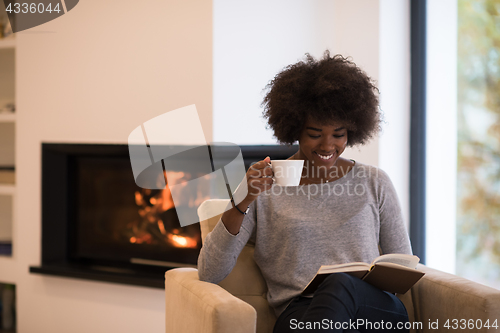 Image of black woman reading book  in front of fireplace