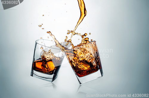 Image of Two whiskey glasses clinking together on gray