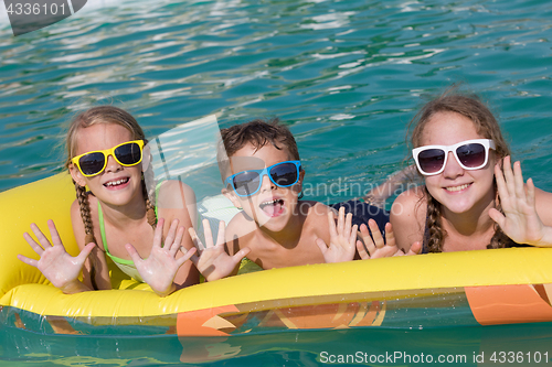 Image of Three happy children playing on the swimming pool at the day tim