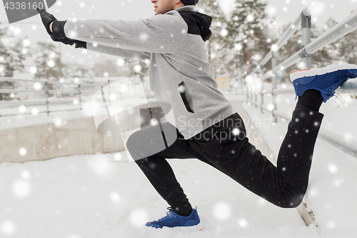 Image of sports man stretching leg at fence in winter