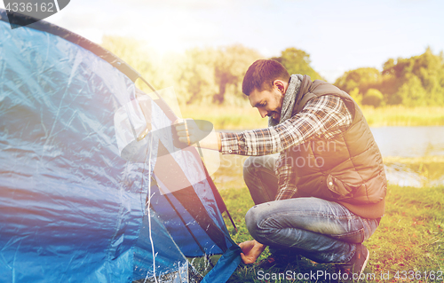 Image of happy male traveler setting tent up outdoors