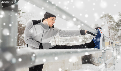 Image of sports man stretching leg at fence in winter