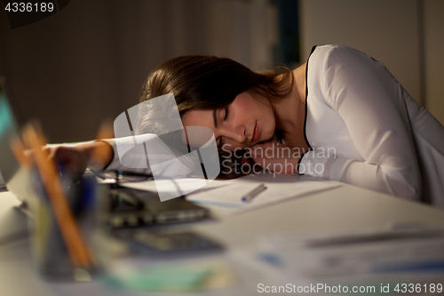 Image of tired woman sleeping on office table at night