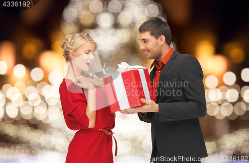 Image of happy couple with gift over christmas tree lights