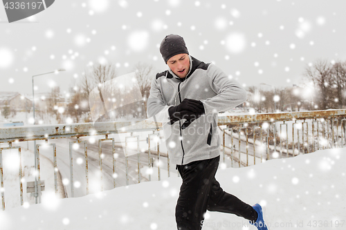 Image of man with earphones running along winter bridge