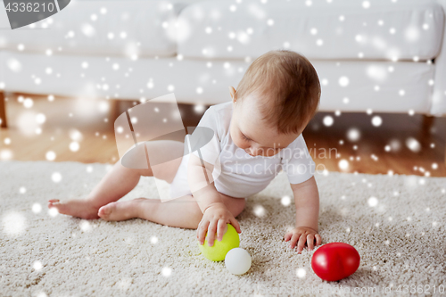 Image of happy baby playing with balls on floor at home