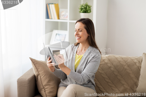 Image of happy woman with tablet pc and bank card at home