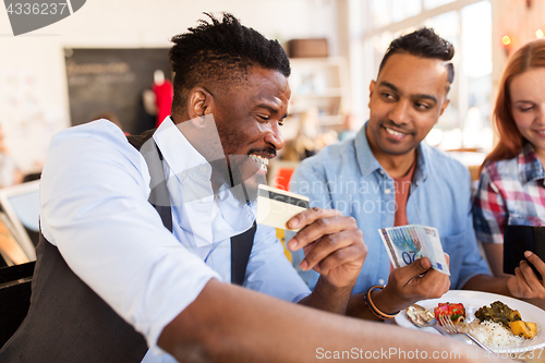 Image of happy friends with money paying bill at restaurant