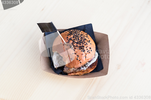 Image of Hamburger on wooden table, one bite taken out of it.