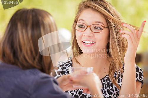 Image of Two Mixed Race Girlfriends Talking Over Drinks Outdoors