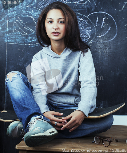 Image of young cute teenage girl in classroom at blackboard seating on ta