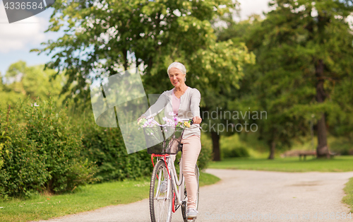 Image of happy senior woman riding bicycle at summer park