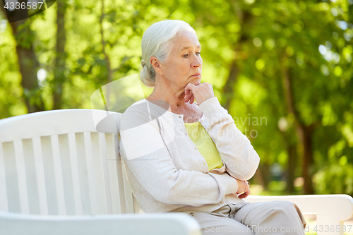 Image of sad senior woman sitting on bench at summer park