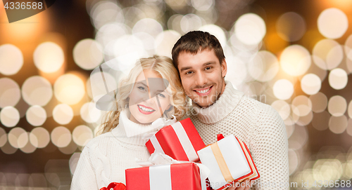 Image of happy couple in sweaters holding christmas gifts