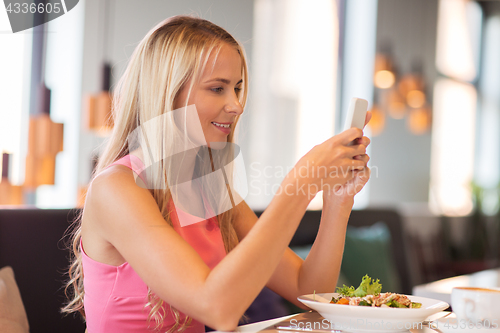 Image of happy woman with smartphone eating at restaurant