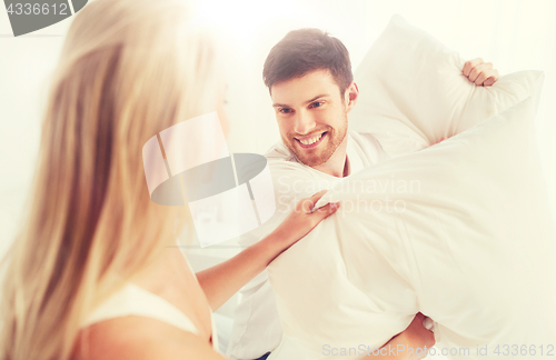 Image of happy couple having pillow fight in bed at home