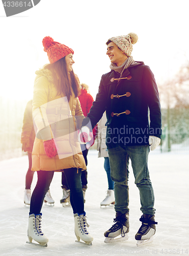 Image of happy friends ice skating on rink outdoors