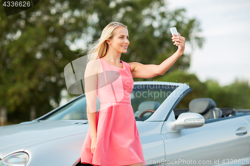 Image of woman posing at convertible car and taking selfie
