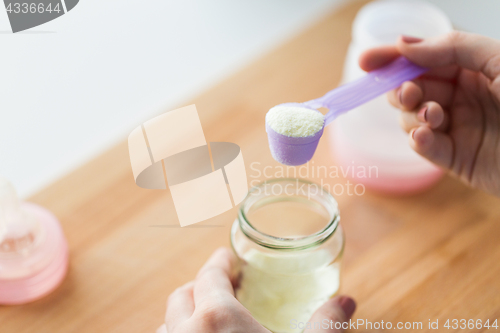 Image of hands with jar and scoop making formula milk