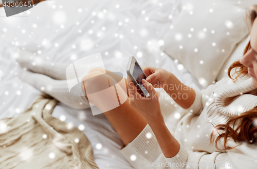 Image of happy young woman with smartphone in bed at home