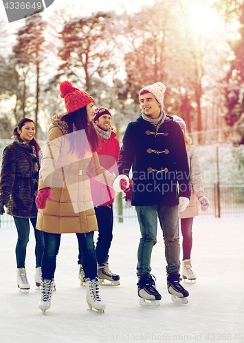 Image of happy friends ice skating on rink outdoors