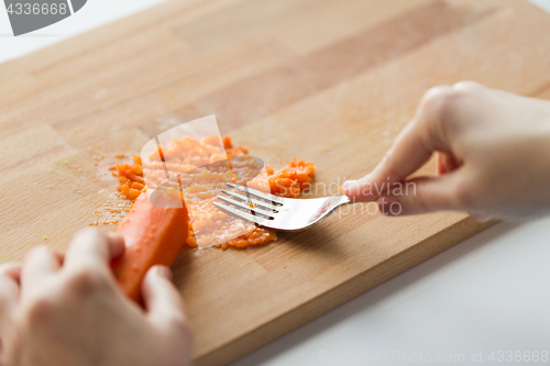 Image of hand with fork making mashed carrot on board