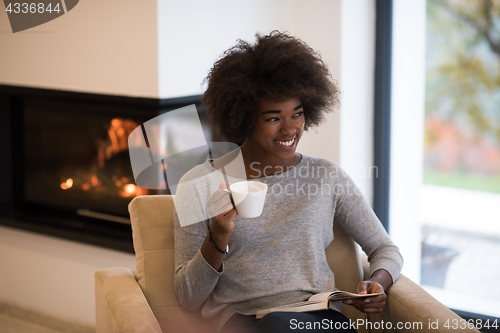 Image of black woman reading book  in front of fireplace