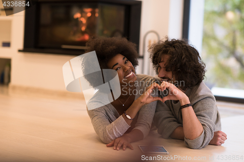 Image of multiethnic couple showing a heart with their hands on the floor