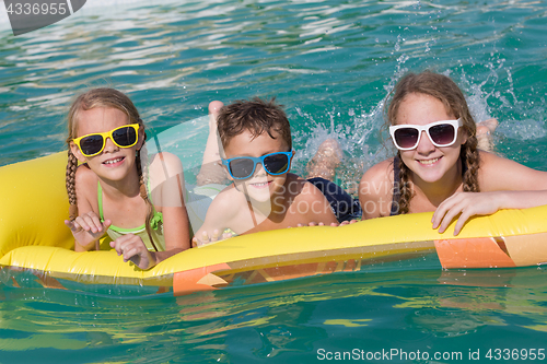 Image of Three happy children playing on the swimming pool at the day tim