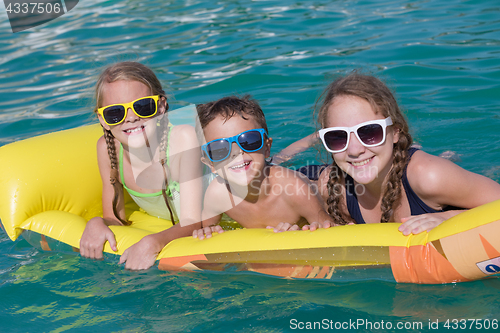 Image of Three happy children playing on the swimming pool at the day tim