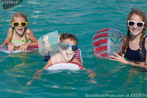 Image of Three happy children playing on the swimming pool at the day tim