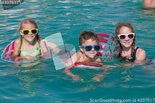 Image of Three happy children playing on the swimming pool at the day tim