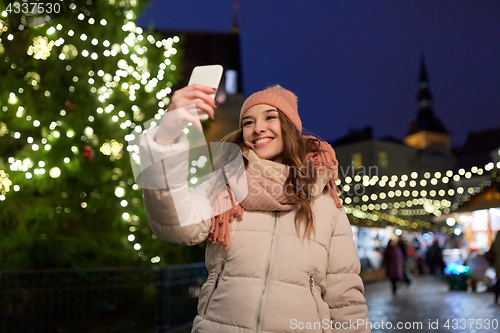 Image of young woman taking selfie over christmas tree