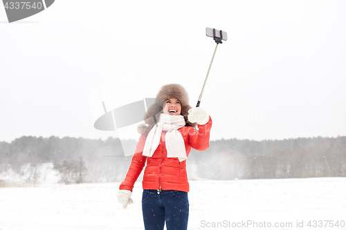 Image of happy woman with selfie stick outdoors in winter