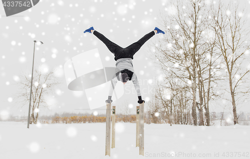 Image of young man exercising on parallel bars in winter