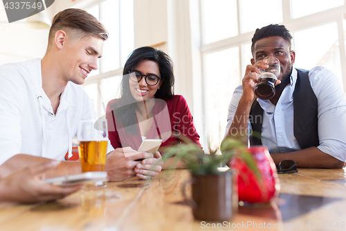 Image of happy friends with smartphone drinking beer at bar